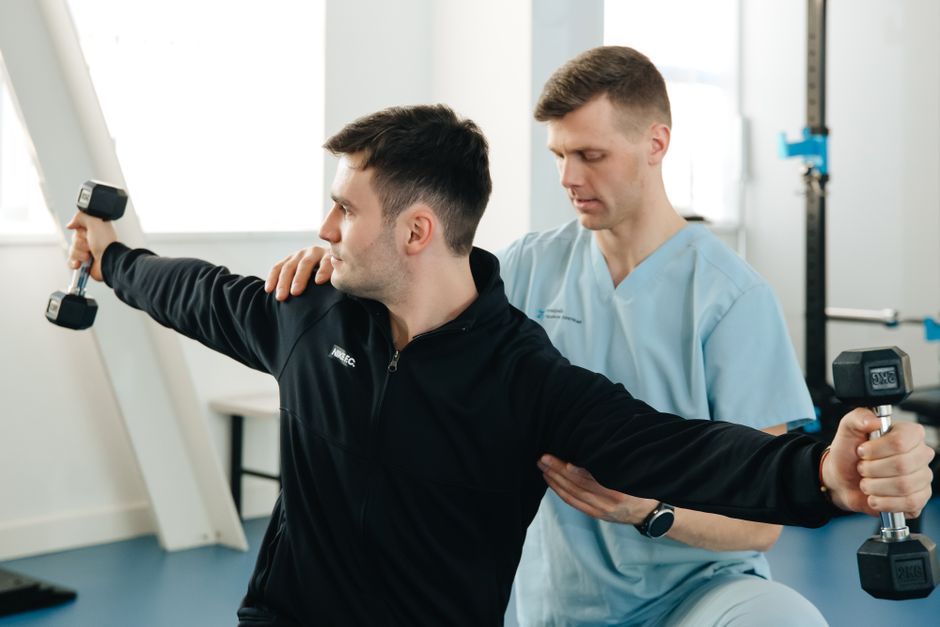 A physiotherapist supporting a patient through a shoulder exercise with dumbbells