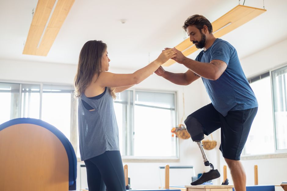 A therapist steadying a man with a prosthetic leg as he stands and balances